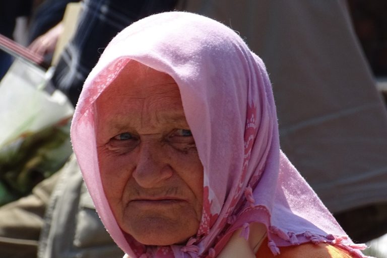Літня жінка в рожевій хустці на площі у Львові