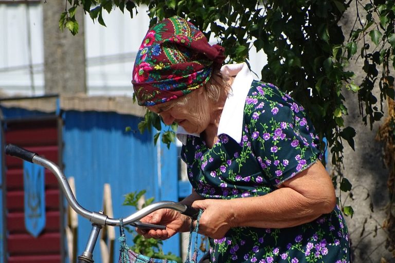 Літня жінка з велосипедом на вулиці села Диканька на Полтавщині